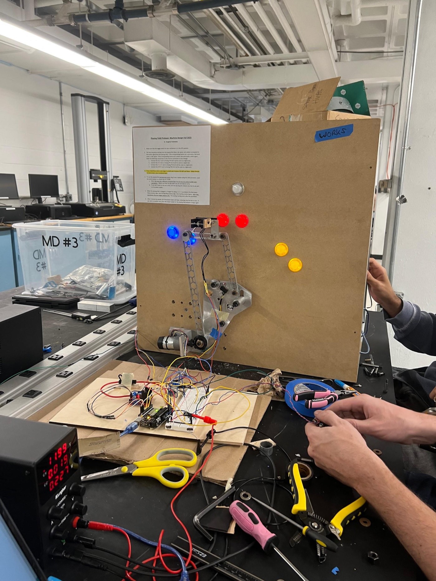 The linkage mid-run during final testing, reaching toward a button on the game board.